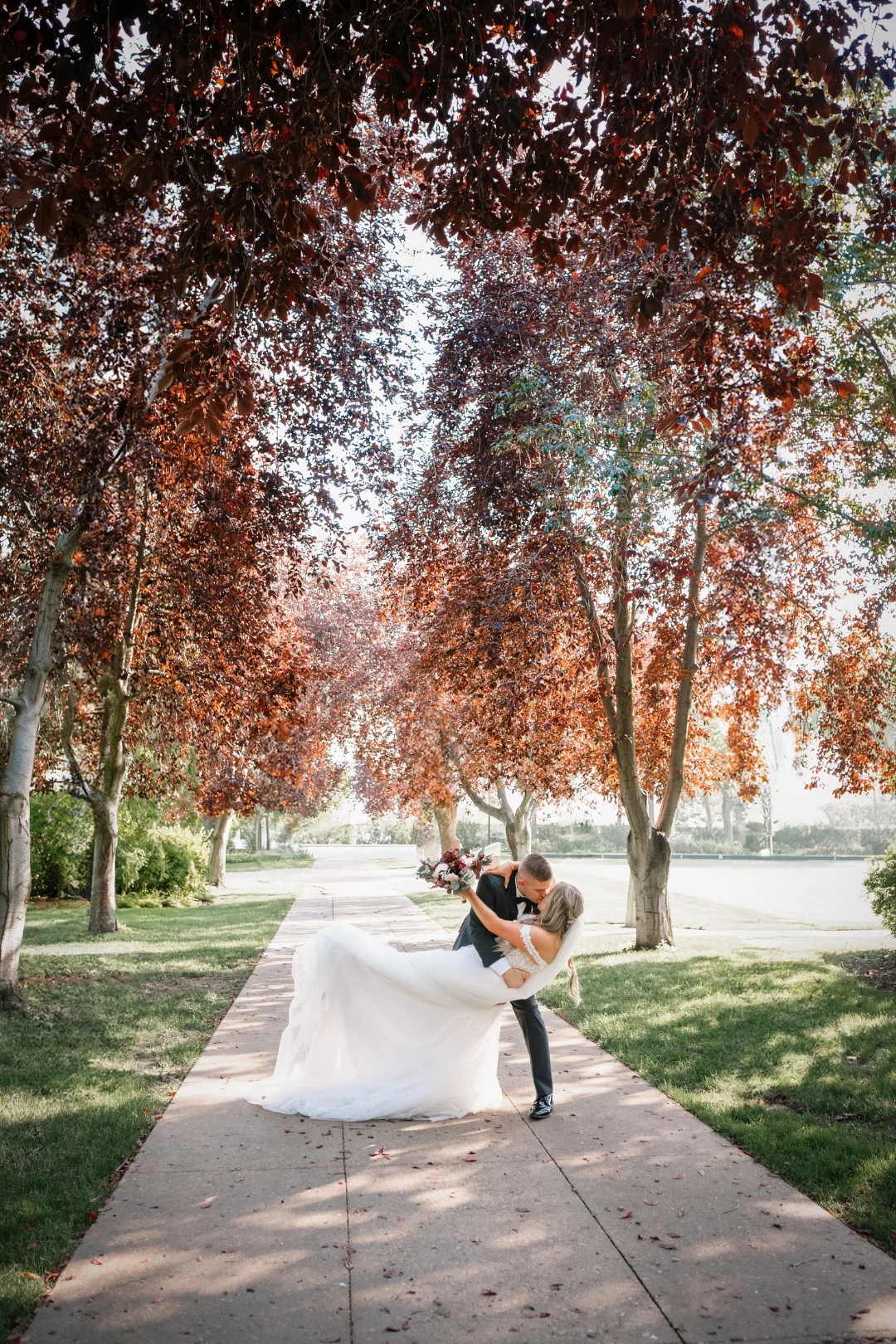 Bride and Groom dip kiss during wedding formals surrounded by lush trees at the Legislature Grounds in Edmonton Alberta. Photo Taken by Pulse Productions Inc.