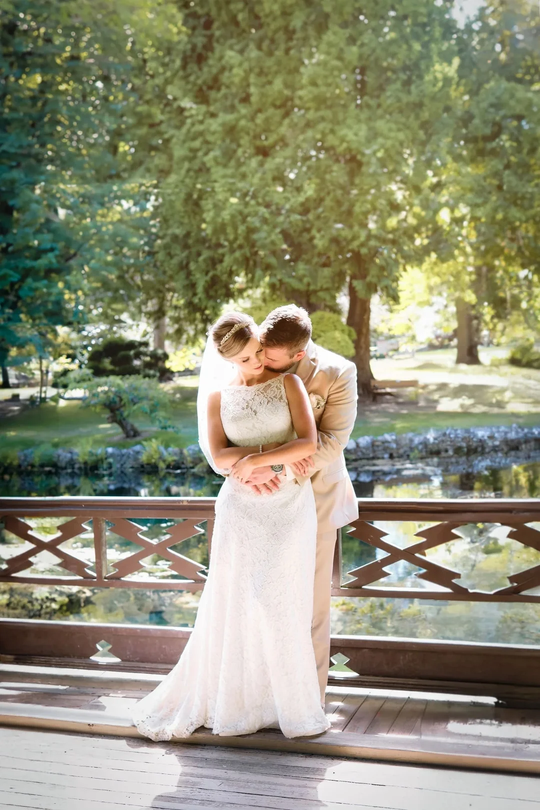Groom embraces Bride from behind while both of them are leaning up against a rail in the Japanese Garden at Hatley Castle in Victoria BC. Photo Taken by Pulse Productions Inc.